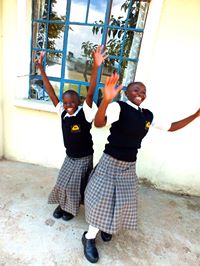 Two WISER girls put their hands high in the air, smiling and about to jump in the air.