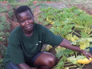 A girl is crouched down in front of a field of plants and is holding a vegetable.