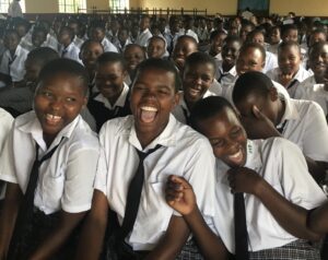 A large group of WISER girls laughing amongst one another, as they sit in an assembly.