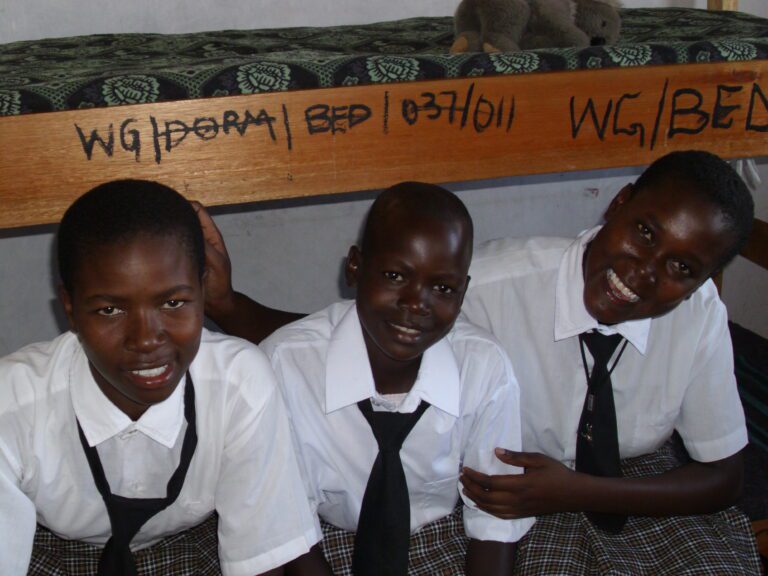 Three WISER girls sit on the bottom bunk of a bed.